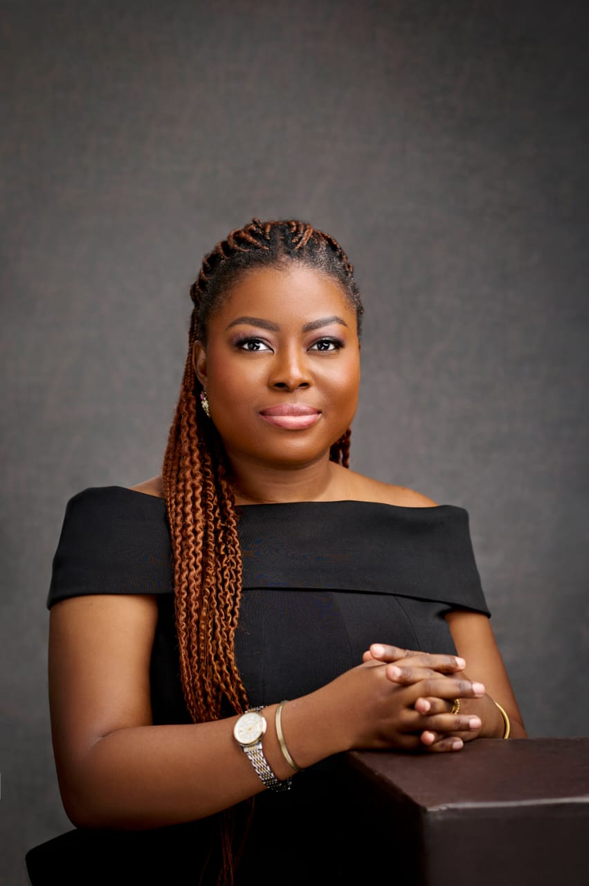 Seated studio portrait of Joan Adu in a black dress against a charcoal background.